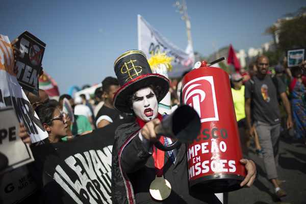 A demonstrator in a costume depicting a banker and holding a replica of a fire extinguisher for putting out the "flame" of an imitation Olympic torch on the route of the Olympic torch, at the Copacabana beach, in Rio de Janeiro, Brazil, August 5.